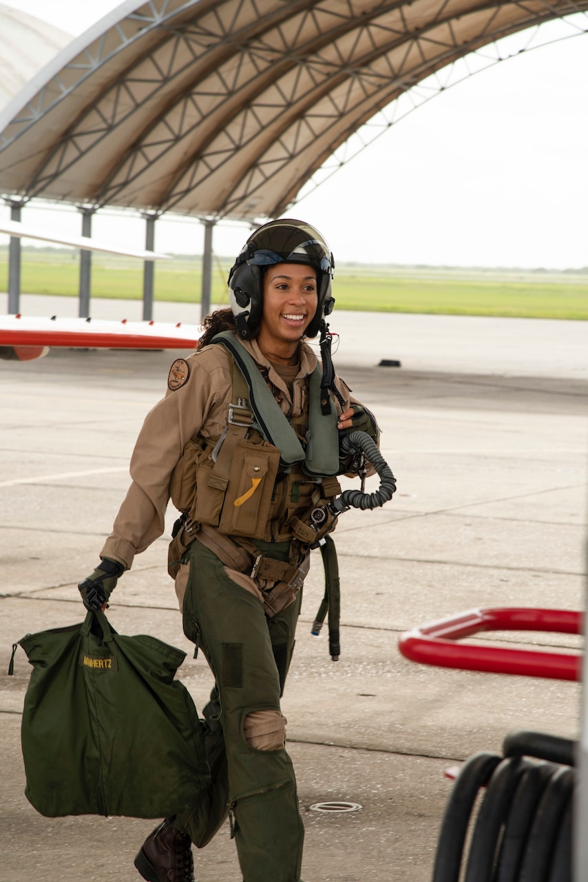 A woman in pilot’s gear walks in a hangar.