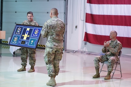 Alaska Army National Guard Maj. Michael Riley, 38th Troop Command adjutant, presents Col. Joel Gilbert, former 38th TC commander, with a gift during an Aug. 2, 2020, change-of-command ceremony at Joint Base Elmendorf-Richardson. Lt. Col. Tim Brower (right) succeeded Gilbert during the ceremony. (U.S. Army National Guard photo by Capt. David Bedard/Released)