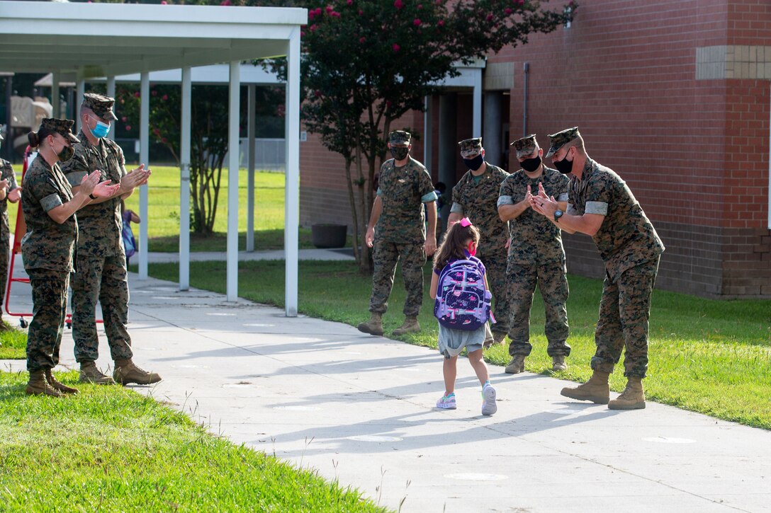 Service members wearing face masks clap to welcome a student back to school.