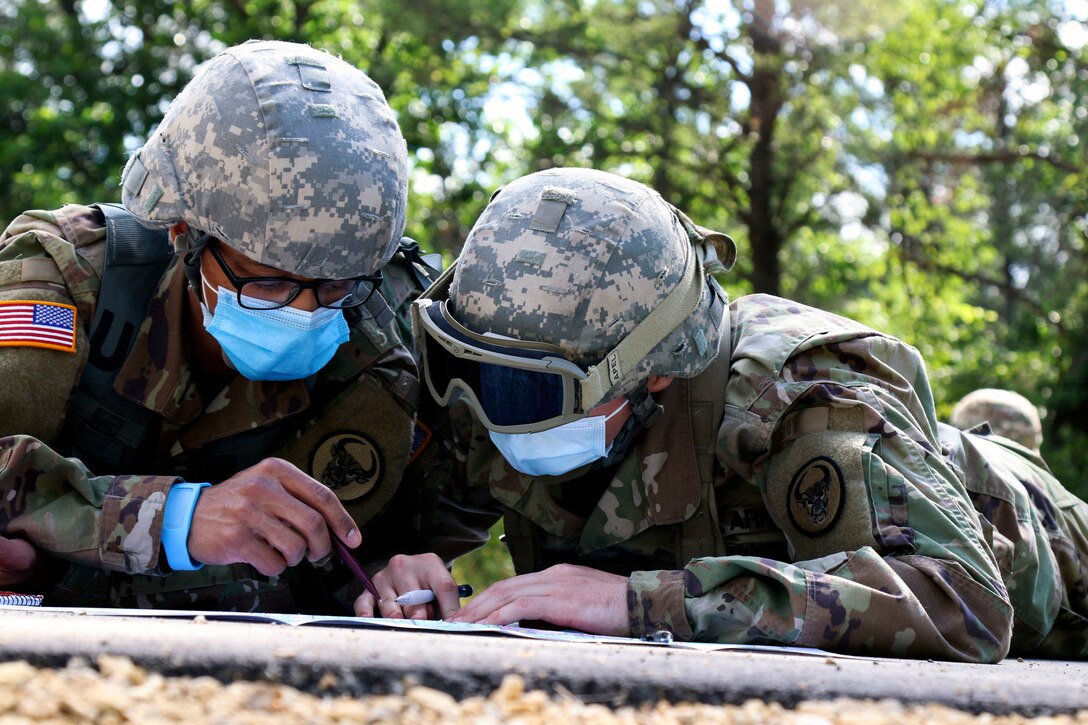 Two soldiers wearing face masks lie on the ground looking at a map.