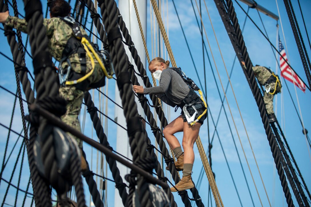 A service member climbs the shrouds of an old ship.