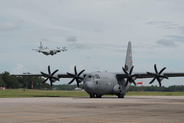 A large plane taxis on a runway while another flies away.