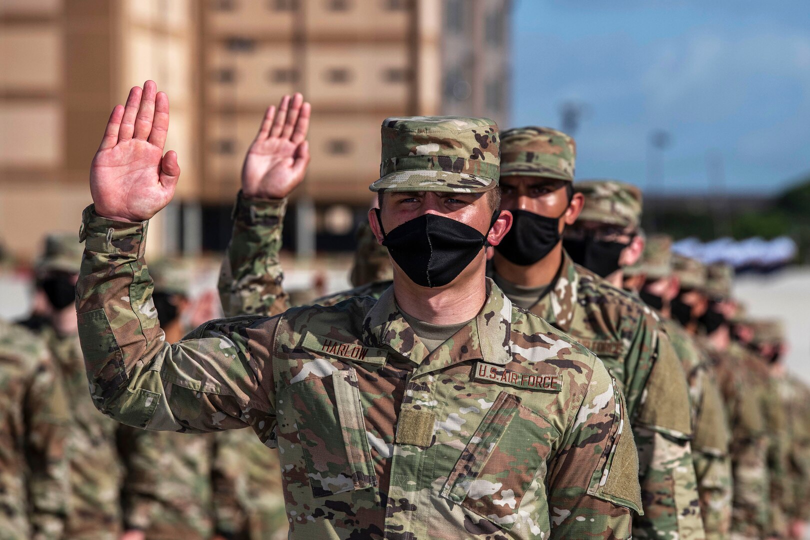 Service members wearing face masks stand in a line with their right hands raised.