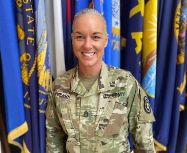 Female Soldier stands in uniform in front of flags