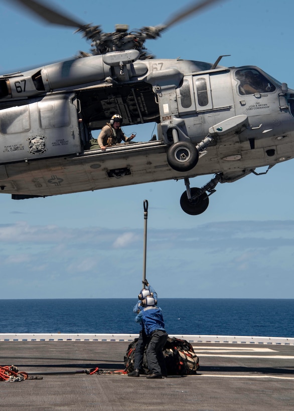 Sailors attach cargo to a hovering helicopter.