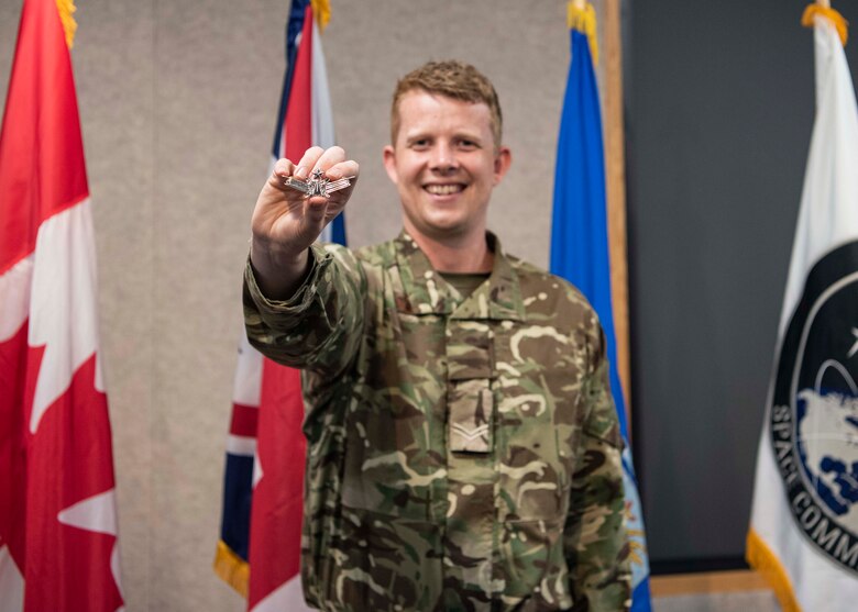 Photo of Cpl Mitchell Astbury holding up the Space Operations Badge he earned