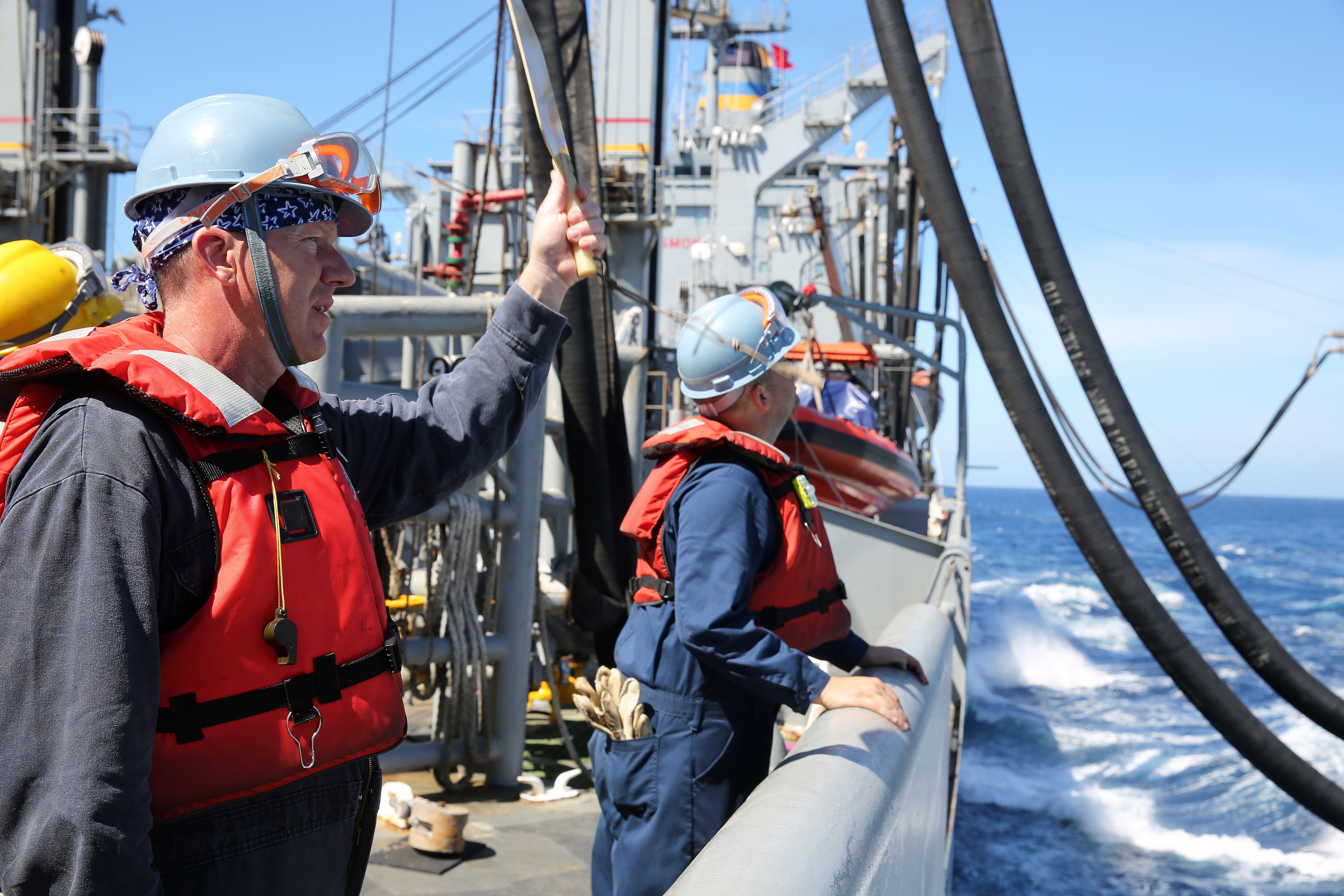Civilian mariner Ryan Berry with the engine utility department of fleet replenishment oiler USNS John Ericsson (T-AO 194) signals to the crew of fast combat ship USNS Rainier (T-AOE 7) during a replenishment at sea operation