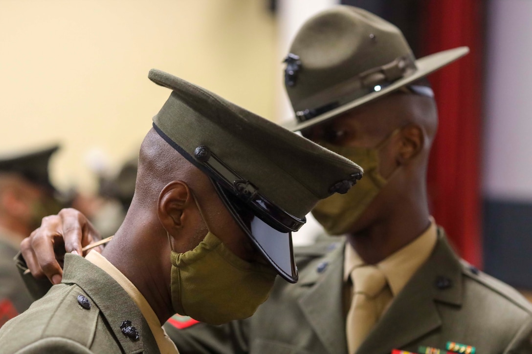 A Marine looks at another Marine’s uniform, while both wear face masks.