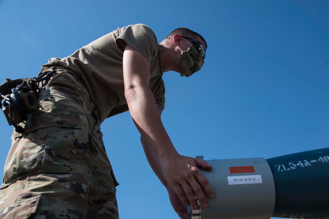 An airman wearing a face mask works on a munition.