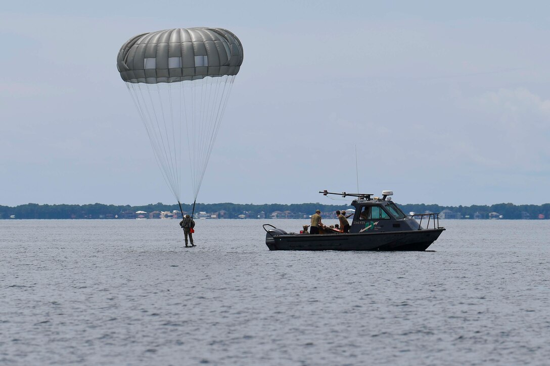 An airman descends into water wearing a parachute.