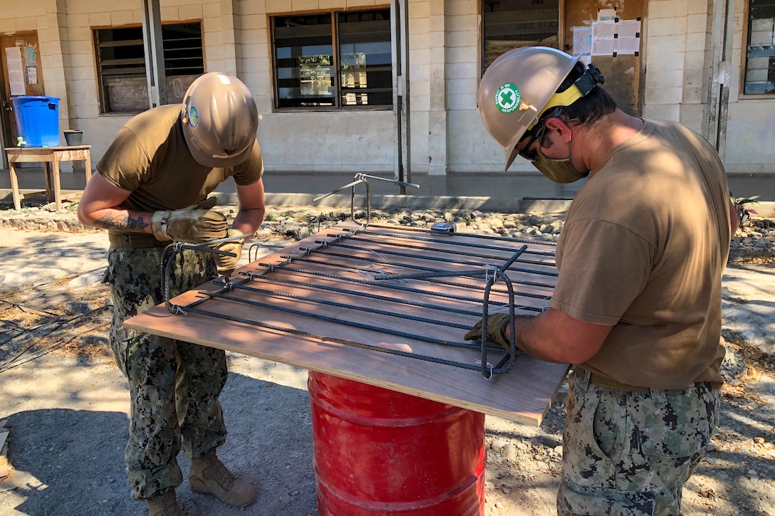 Two sailors tie rebar during a construction project.