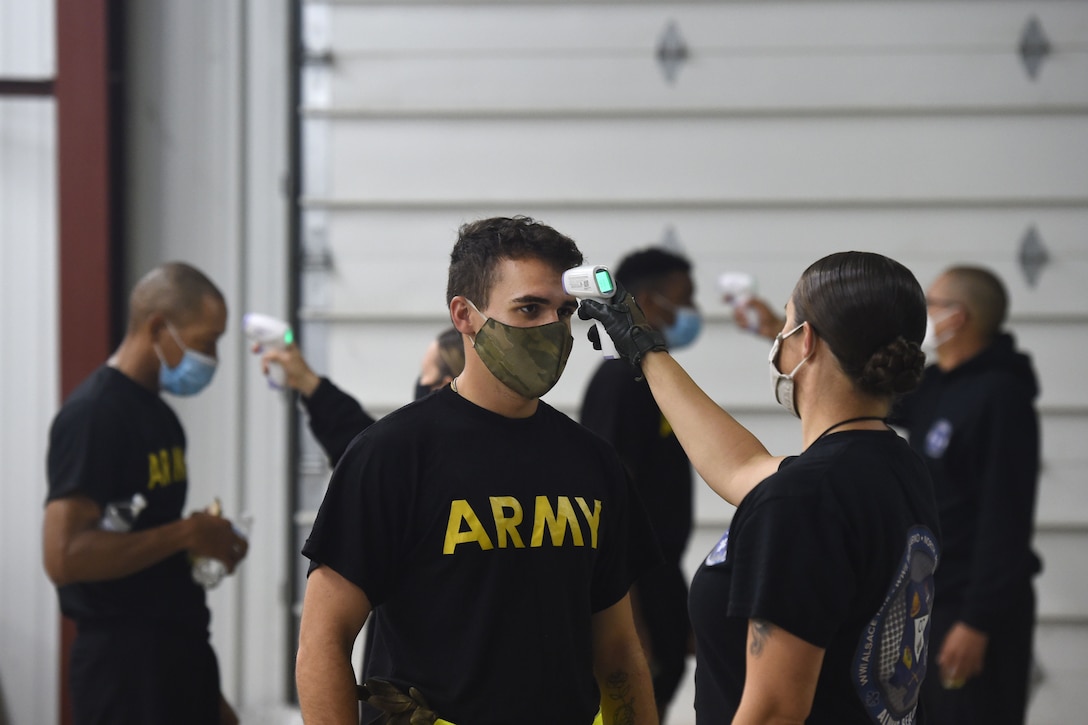 A soldier wearing a face mask gets his temperature checked by another soldier wearing a face mask.
