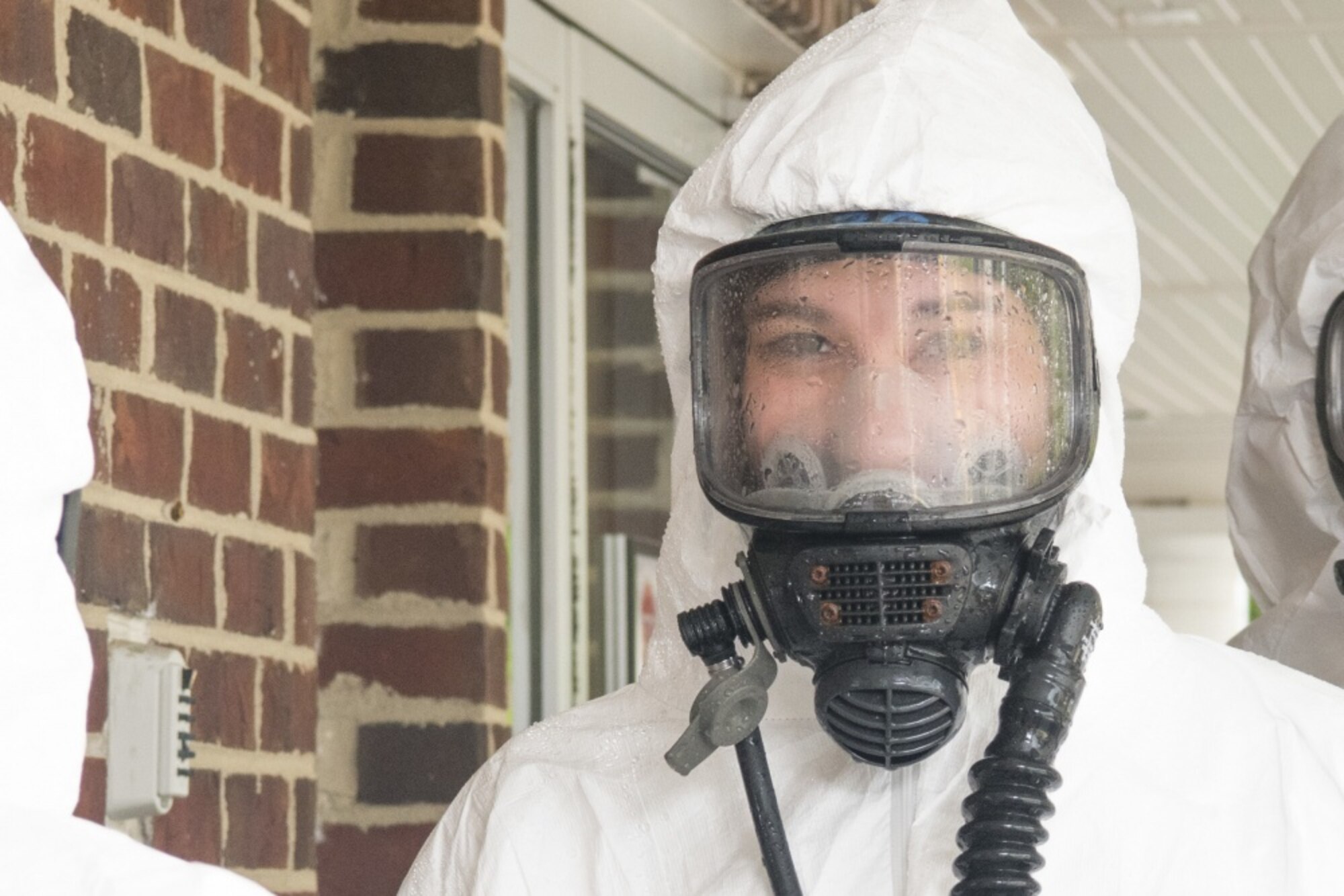 An Airman wears a white personal protective suit and gas mask