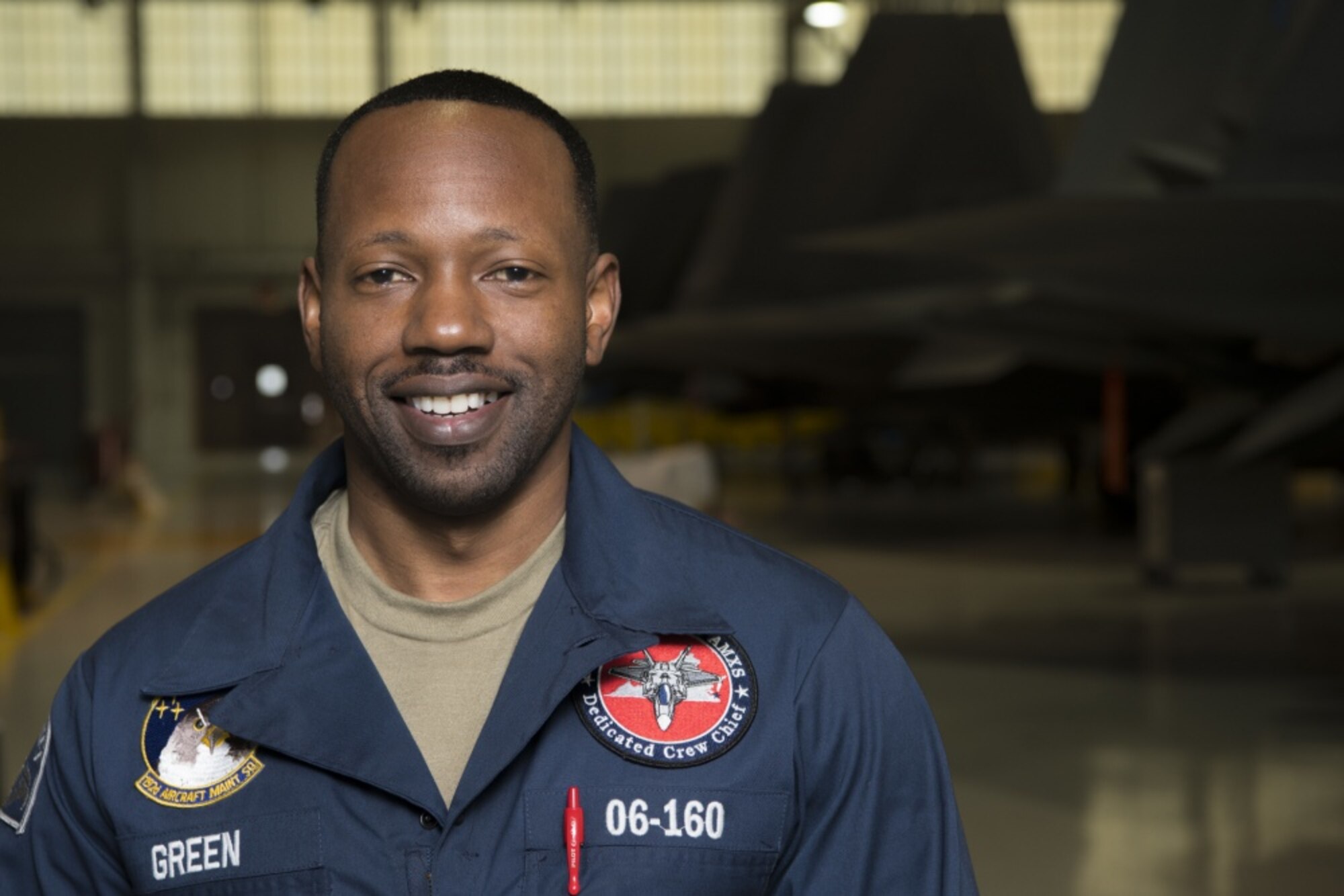 An Airman wearing a blue coverall suit smiles for the camera