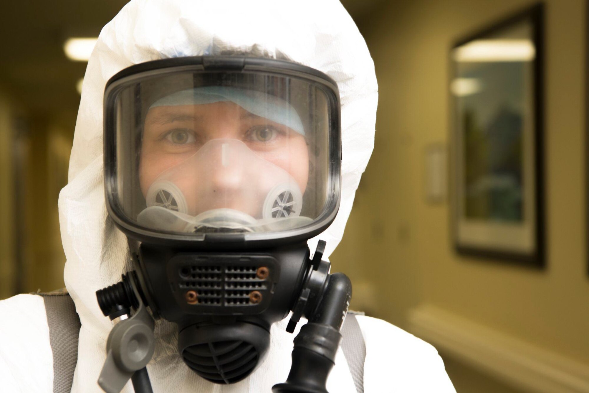 A woman wearing a personal protective suit and gas mask looks at the camera