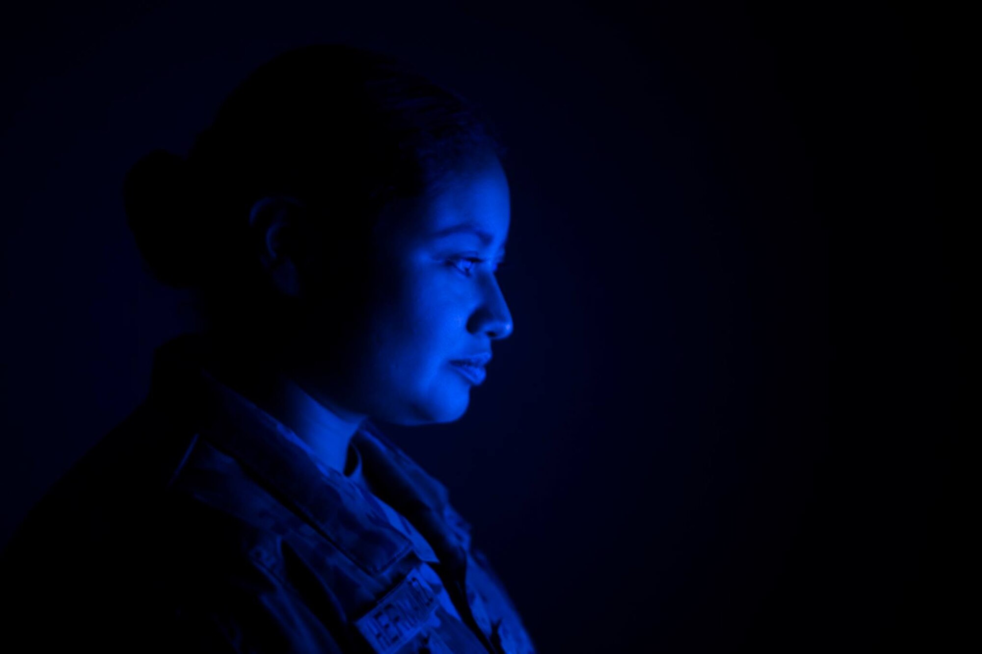 A blue light shines on an Airman's face as she looks at a computer screen