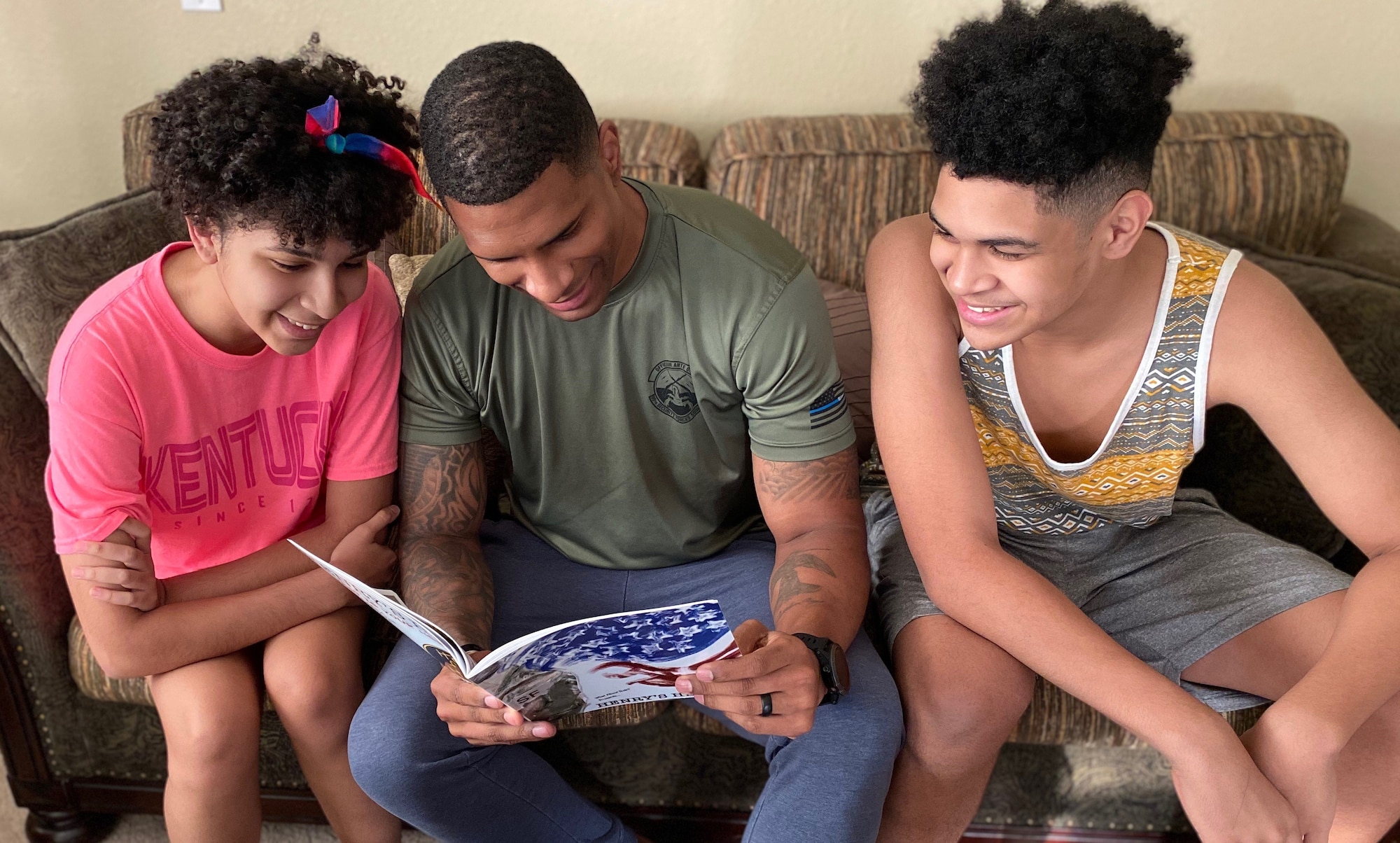 A security forces Defender flips through a copy of Henry's Hero with his children.