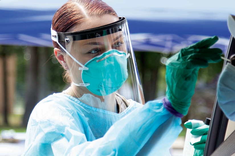 A soldier wearing personal protective equipment conducts a drive-thru COVID-19 test.