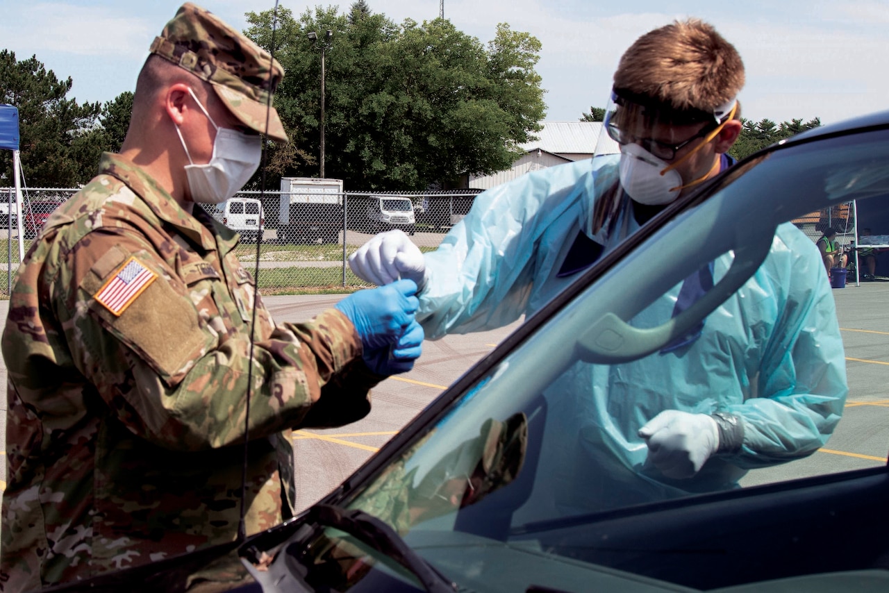Soldiers wearing masks and personal protective equipment conduct drive-thru COVID-19 tests.