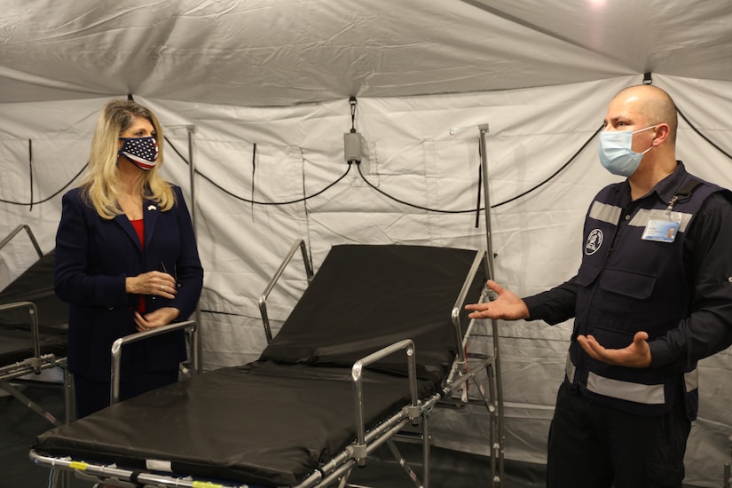 Ambassador Sharon Day, wearing a mask, stands inside a donated field hospital.