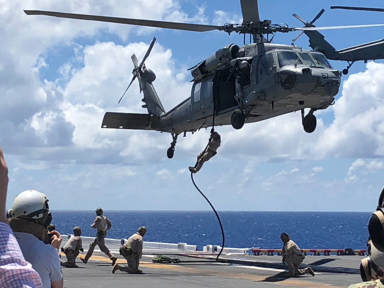 Sailors slide down a rope from a helicopter onto the flight deck of a ship.