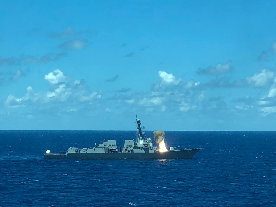 A ship floating in blue water fires a missile.