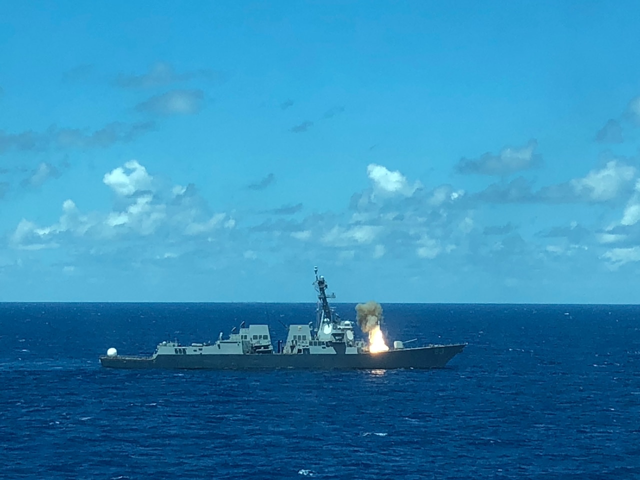 A ship floating in blue water fires a missile.
