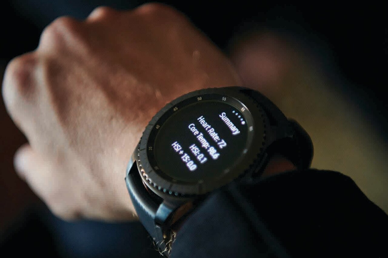 A hand wears a wristwatch with a digital display that shows heart rate and core temperature.