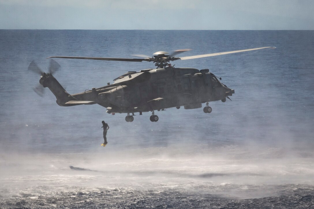 A service member jumps from a helicopter into a body of water.