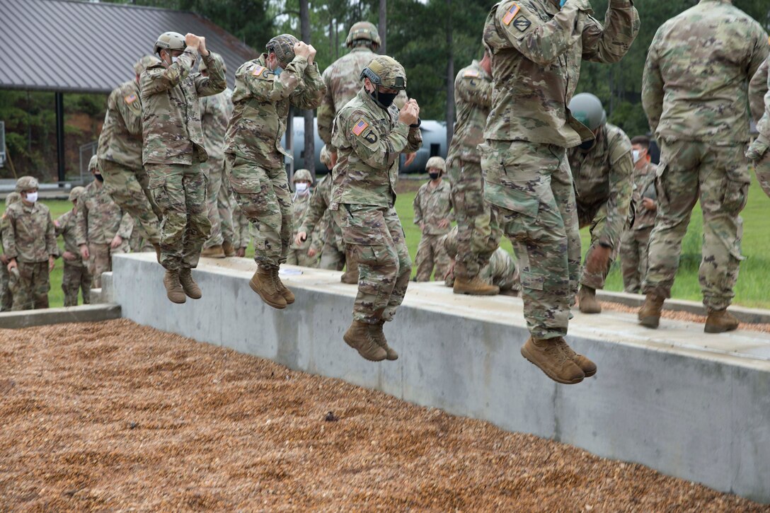Soldiers standing in a line jump from a concrete block.