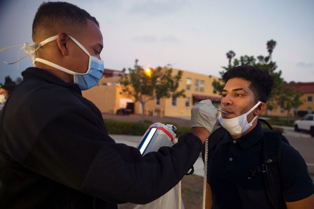 A Marine wearing a face mask screens a recruit wearing a face mask.