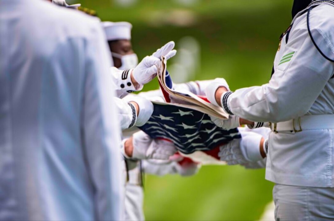 Service members wearing protective gear fold the American flag.