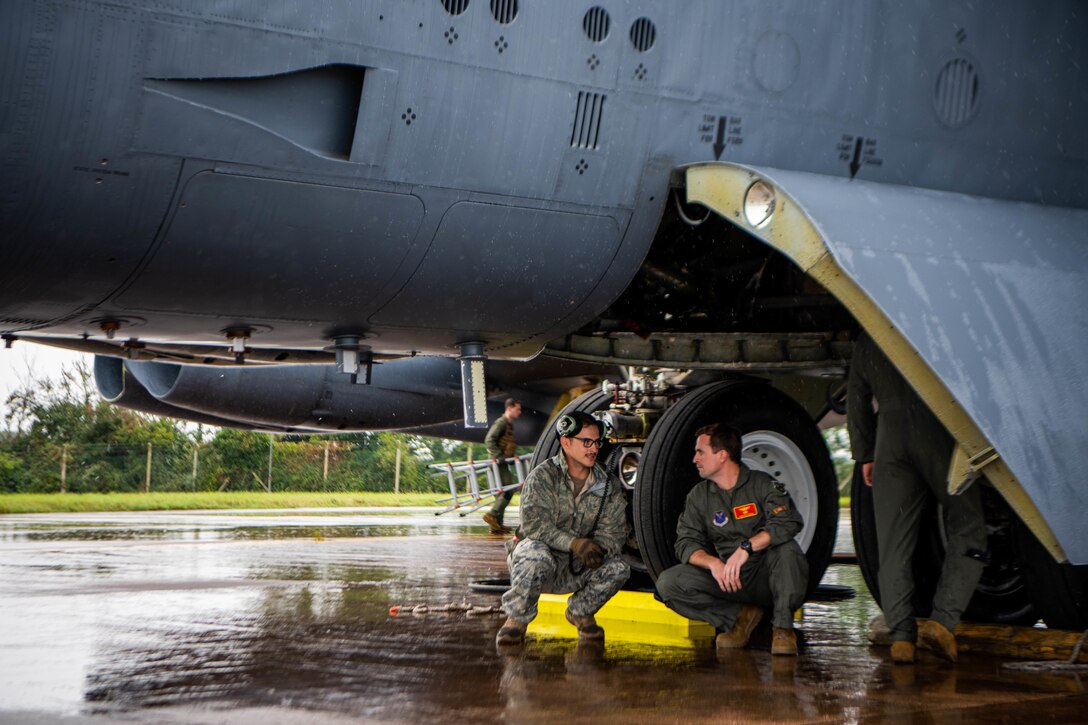 Two males sitting under a military aircraft talking