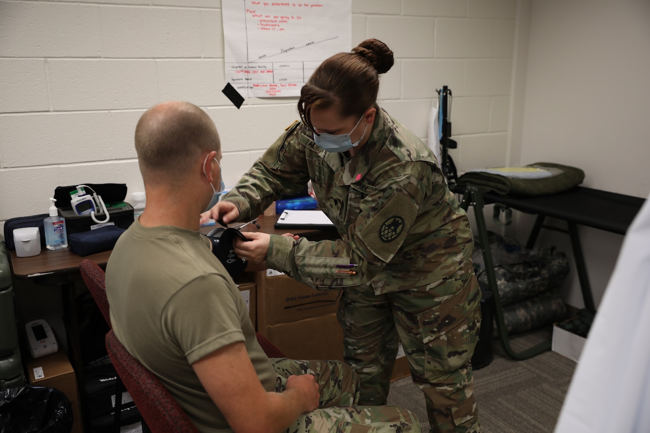 A soldier wearing a face mask checks another soldier’s blood pressure.