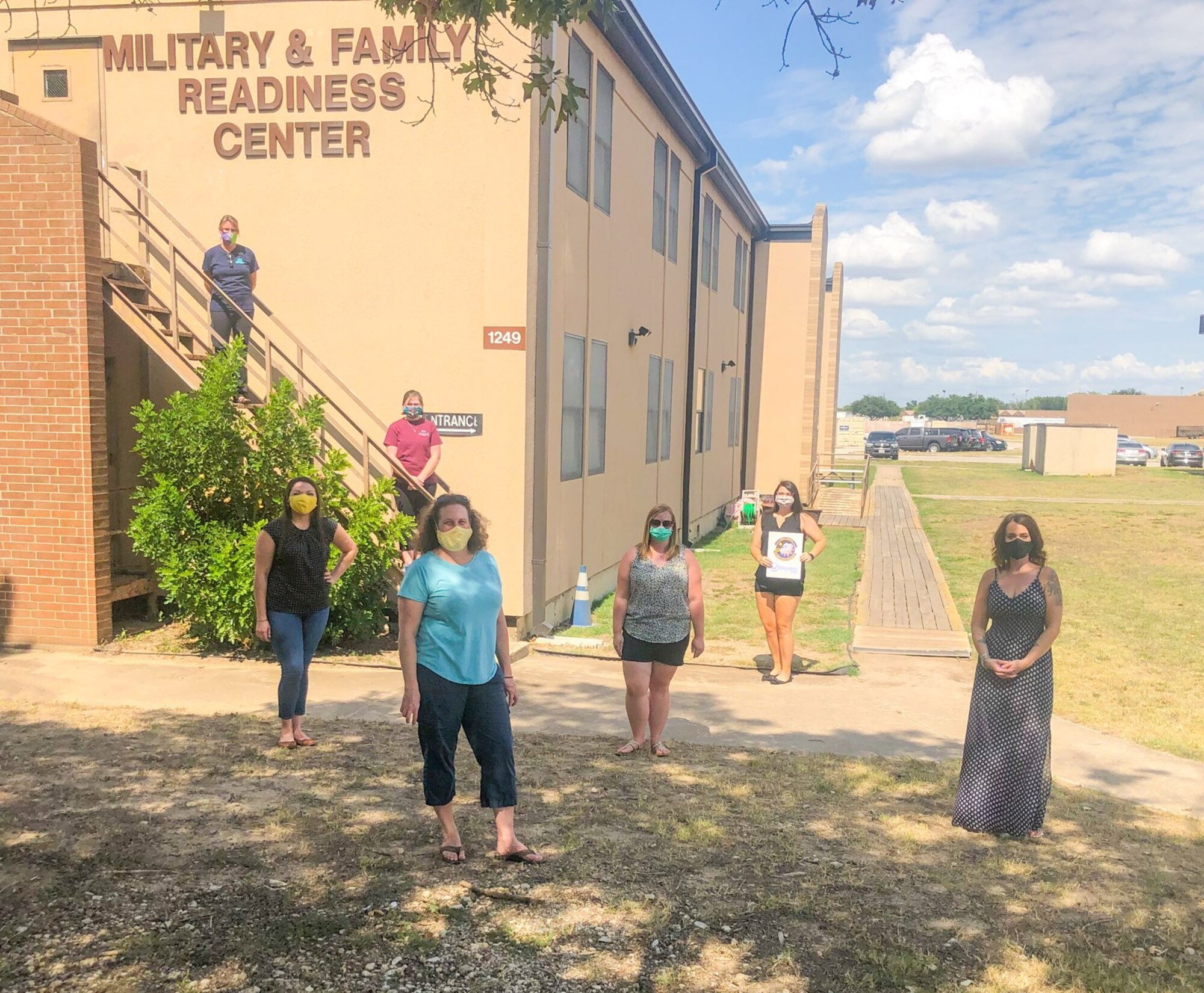 Women stand near a building with masks on and six feet apart.