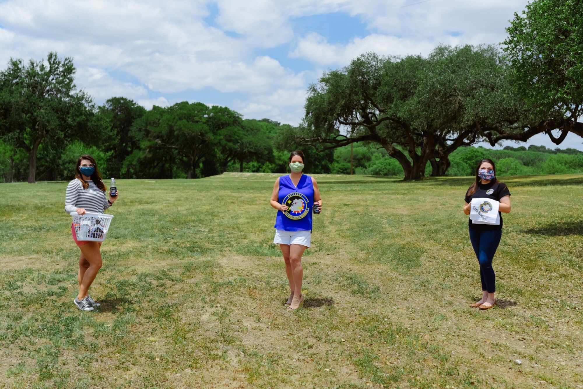 Three women with masks standing six feet apart holding unit gear.