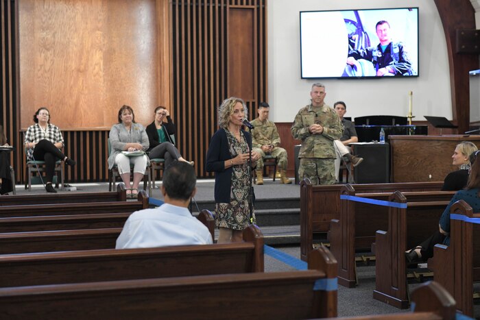 Photo shows woman standing at mic stand addressing audience.