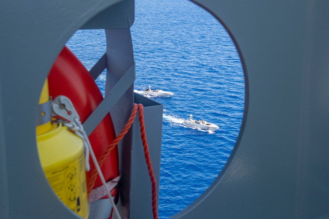 Two small boats are visible in blue waters through an open circle on a ship's structure.