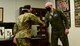 A photo of an officer receiving a coin from a general.