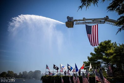 Firetruck spraying water over a lake with flags displayed on an overlook.