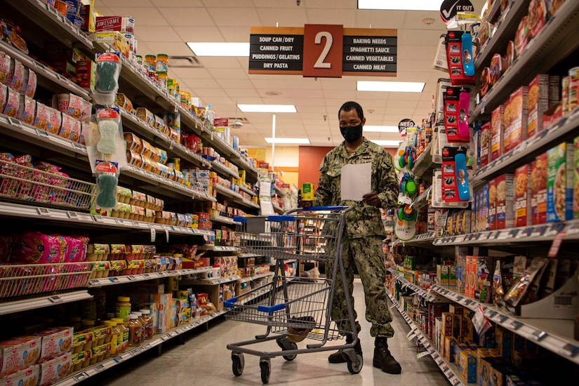 A sailor wearing a face mask shops in a grocery store.