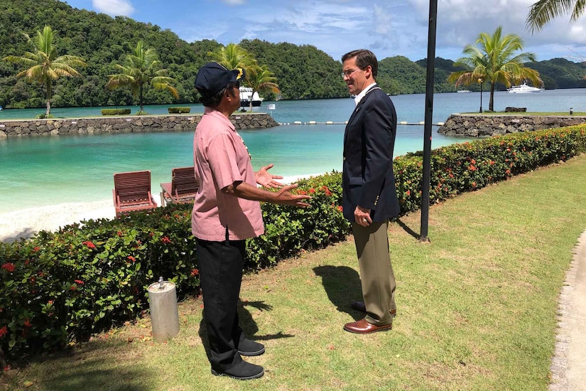 Two men have a discussion near a body of water.