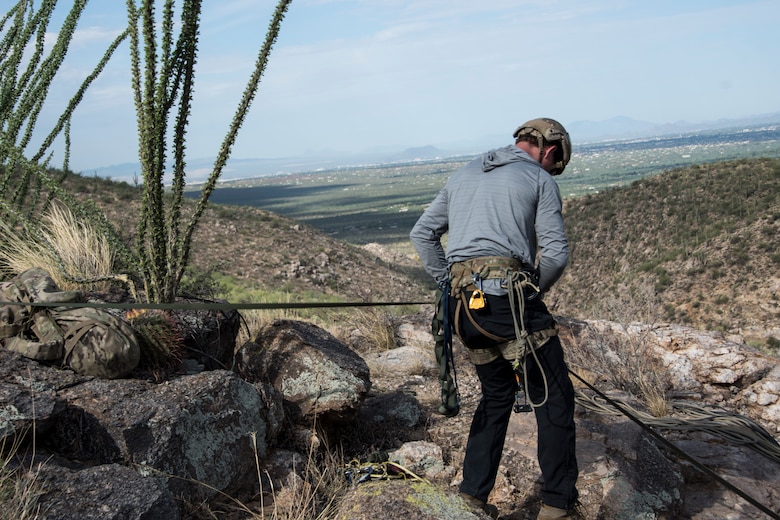 A photo of an Airman rappelling down a rock
