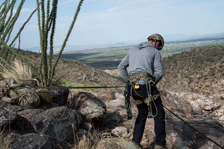 A photo of an Airman rappelling down a rock