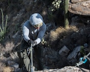 A photo of an Airman rappelling down a rock