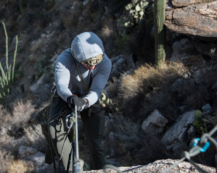 A photo of an Airman rappelling down a rock