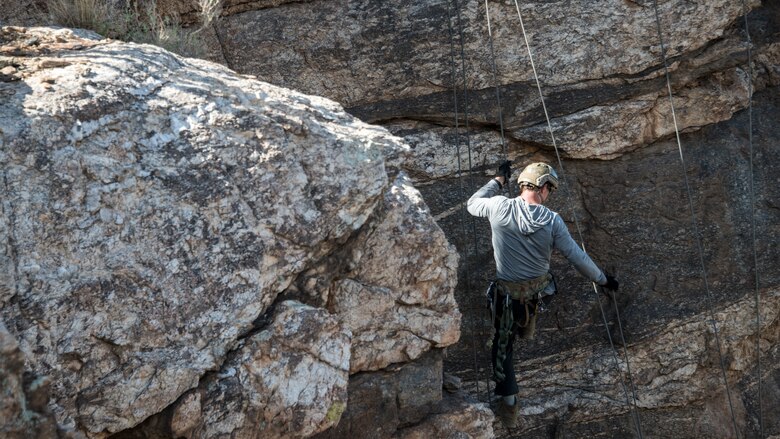 A photo of an Airman rappelling down a rock
