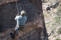 A photo of an Airman rappelling down a rock
