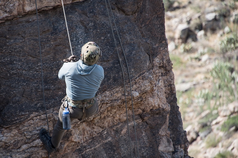 A photo of an Airman rappelling down a rock