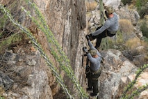 A photo of an Airman rappelling down a rock